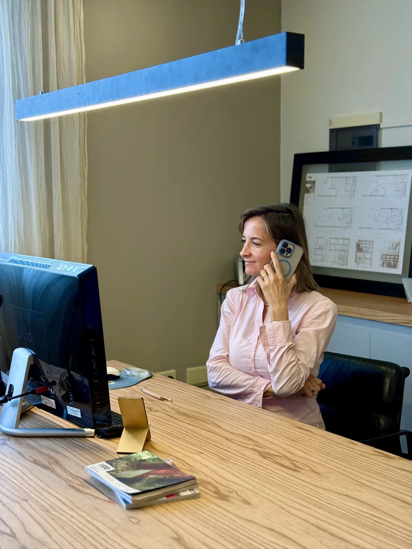 Glint team member on a call at her desk with architecture plans in the background